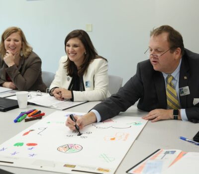 Man draws on notepad while female counterparts look on